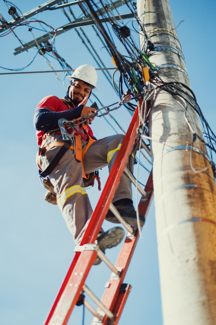 Crafting Captivating Headlines: Your awesome post title goes here Electrician safely repairing electrical lines on a ladder under clear blue sky.